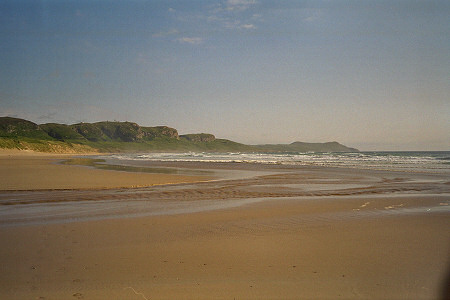 Picture of a beach in a bay with cliffs in the background, bathed in a golden sunshine
