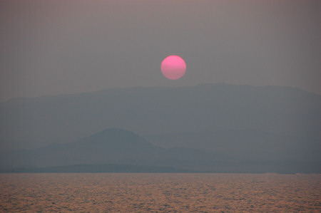 Picture of a red sun setting over a very hazy island