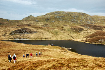 Picture of a group of walkers approaching a loch (lake) with a hill in the background