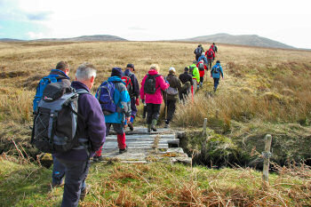 Picture of a group of walkers crossing a makeshift bridge into the open countryside