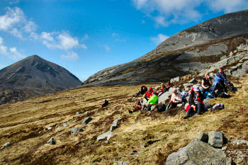 Picture of a group of walkers resting under a background of huge mountains (the Paps of Jura)