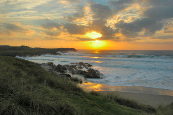 Picture of a beautiful sunset over a bay, waves breaking and cliffs stretching out into the sea