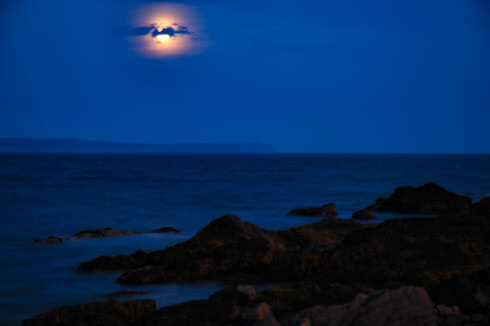 Picture of the moon shining over a sea loch, another part of the island on the other side of the loch