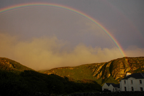 Picture of a rainbow over some rocky crags and a house
