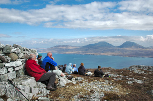 Picture of a group of walkers resting on the top of a hill looking over a sound to another island (from Islay to Jura)
