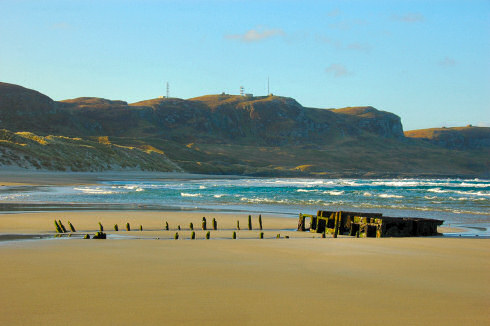 Picture of a ship wreck on a beach, crags in the background