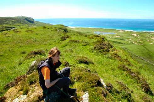 Picture of a young woman sitting on hills high above dunes and the sea