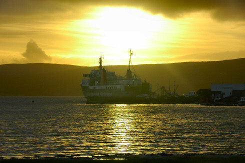 Picture of a sunset behind some hills, a ferry berthed in the foreground