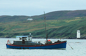 Picture of an old lifeboat now used as a pleasure boat, moored with a lighthouse in the distant background