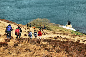 Picture of walkers approaching a lighthouse, the sea below