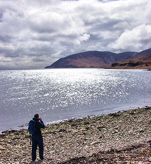 Picture of a man taking a picture of the scenery on the shore of a sound between two islands