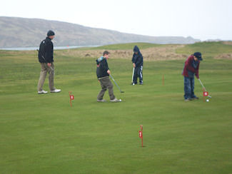 Picture of a group of children practising golf putts under the watchful eyes of a coach