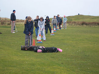 Picture of a group of children practising golf swings under the watchful eyes of a coach