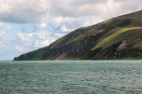 Picture of steep cliffs along a sound, a lighthouse at the end of the cliffs