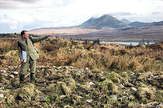 Picture of a head gamekeeper pointing into the distance, some distinctively shaped mountains in the background