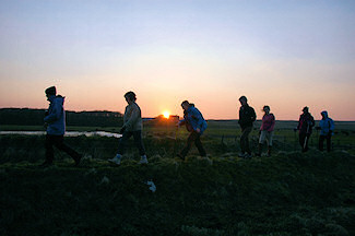 Picture of some walkers on a sea wall with the sun setting in the background