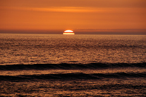 Picture of two waves coming in under the backdrop of an orange-red sunset