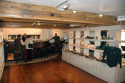 Picture of the Laphroaig distillery visitor centre, people at a bar and some shop shelves with merchandise