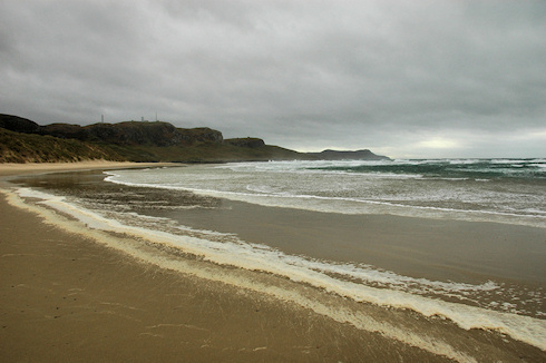 Picture of a wide bay with a sandy beach on a stormy day, foam blowing up on the beach