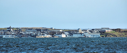 Picture of a coastal village (Bowmore on Islay) seen across a sea loch. Bowmore distillery clearly visible