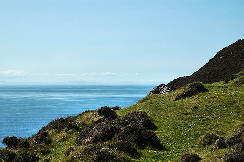 Picture of a view over a heather clad cliff face with land on the other side of a sea strait