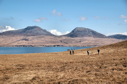 Picture of walkers approaching a sound between two islands, two round shaped hills on the other island