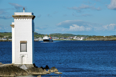 Picture of a ferry leaving a small port, seen from behind a lighthouse