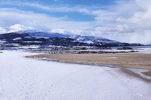Picture of a beach covered in snow, behind it a hillside in snow
