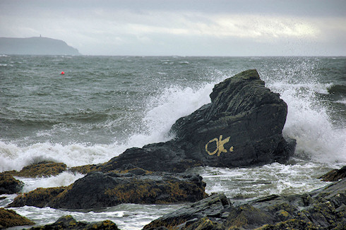 Picture of waves breaking over a rock with the letters 'ok' painted on it