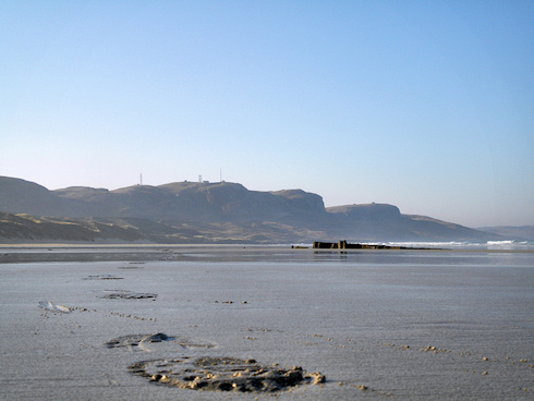 Picture of footsteps on a beach, a wreck and coastal hills in the background