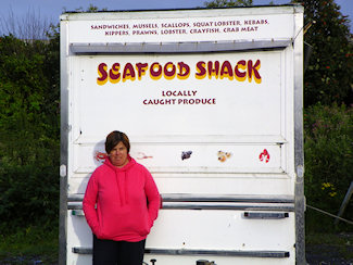 Picture of a trailer with the words Seafood Shack written on it, a woman standing in front of it