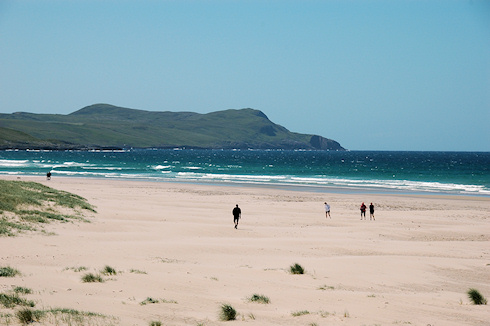 Picture of various people walking on a sandy beach in brilliant summer sunshine