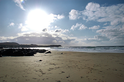 Picture of the sun bursting out behind some clouds of a sandy bay