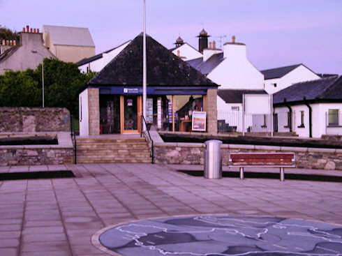 Picture from the centre of a village square, a map of Islay on the floor, tourist office in the background