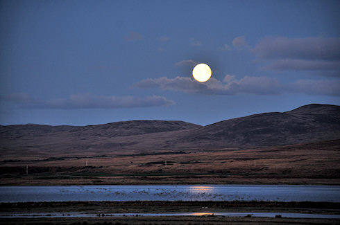 Picture of a moonrise over a sea loch, a hilly ridge behind it