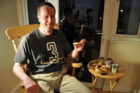 Picture of a man next to a table with scones, clotted cream and jam