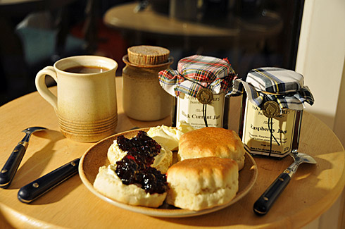 Picture of scones with clotted cream and jam on a plate, glasses of jam behind it