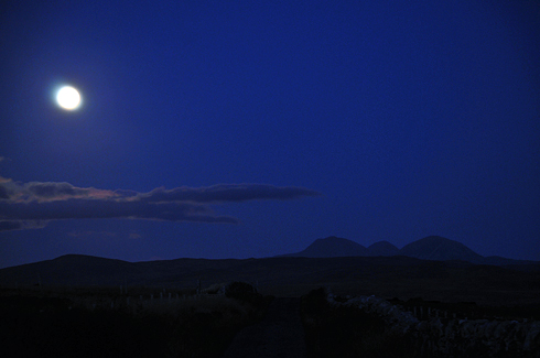 Picture of a moonlit landscape, looking along a road, distinctly shaped mountains in the distance on the right