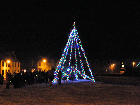 Picture of carol singers standing around a Christmas tree on a coastal village green