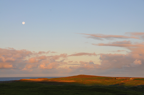 Picture of the moon over an island landscape in the morning sun