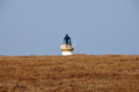 Picture of the top of a lighthouse appearing behind a hill