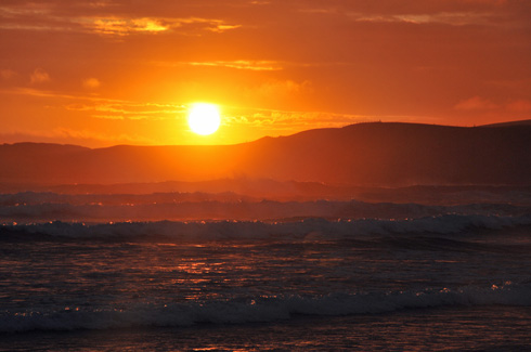 Picture of a sunset with clouds in the sky and waves running into a bay