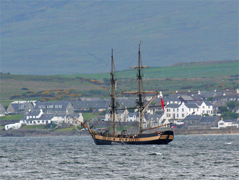 Picture of a tall ship anchored on a sea loch, just off a coastal village