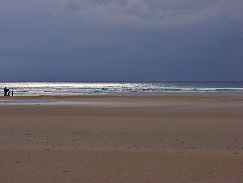 Picture of a beach under dark clouds with the sun breaking through. People on one side