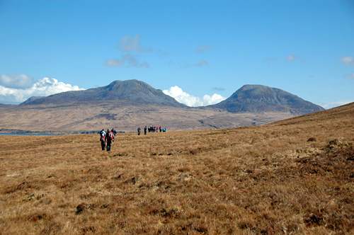 Picture of a group of walkers in a coastal landscape with high hills in the distance