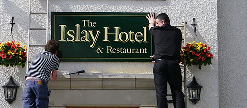 Picture of two men hanging a sign for The Islay Hotel