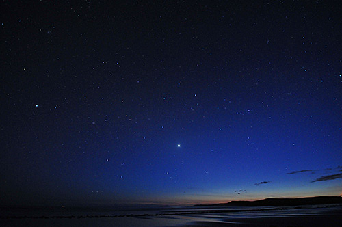 Picture of the sky over a beach in the last light, many stars starting to show
