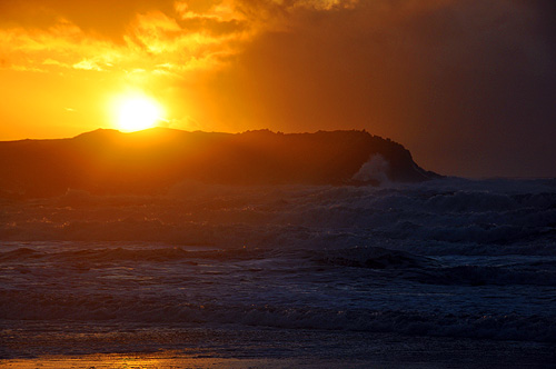 Picture of a colourful sunset over rocks and waves