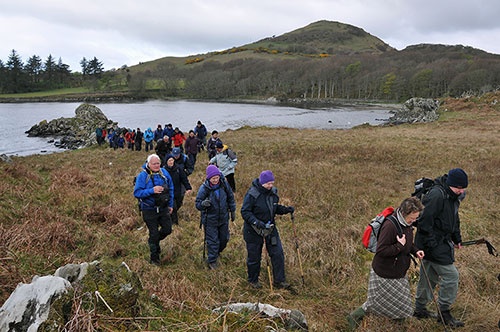 Picture of walkers next to a bay, a hill in the background