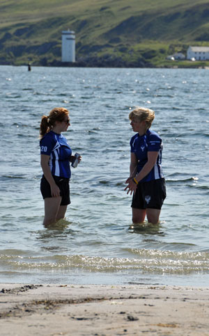 Picture of two female beach rugby players cooling down standing in the water, a lighthouse in the background